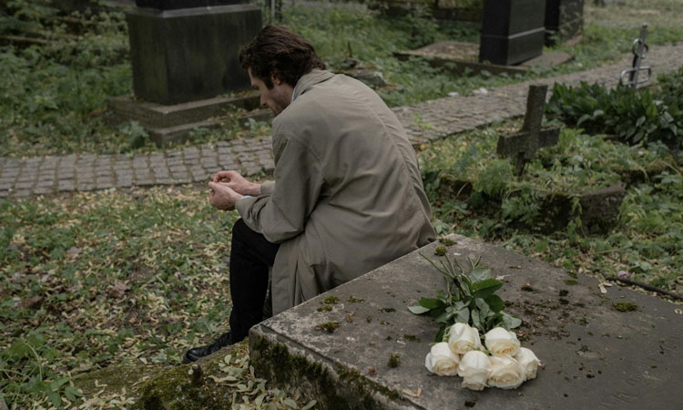 Grieving Person Sitting on a Grave in Cemetery